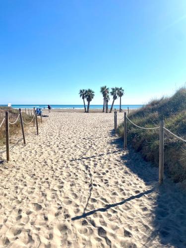 a sandy beach with palm trees in the distance at Lowenva beach apartment in Canet de Berenguer