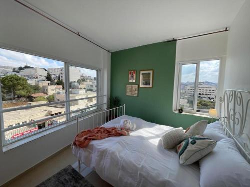 sypialnia z białym łóżkiem, zielonymi ścianami i oknami w obiekcie Zaatar House w mieście Bethlehem