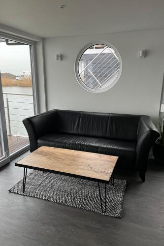 a living room with a black leather couch and a table at Hausboot der Friesländer im Wangermeer in Wangerland