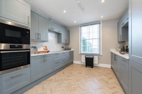 a kitchen with blue cabinets and a large window at Elliot Oliver - Laverham House - Stunning 6 Bedroom Regency House With Parking in Cheltenham