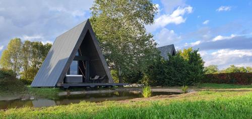 Una pequeña casa con techo negro encima de un estanque. en Héthatár Wellness Vendégház - Gerle, en Pusztavacs