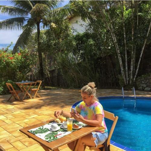 a woman sitting at a table next to a pool at Pousada Chalés Sinbad in Ilhabela