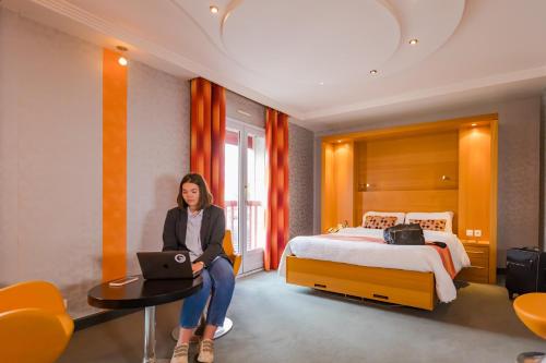 a woman sitting in a hotel room with a laptop at Logis Hôtel Restaurant Le Fruitier in Villedieu-les-Poëles