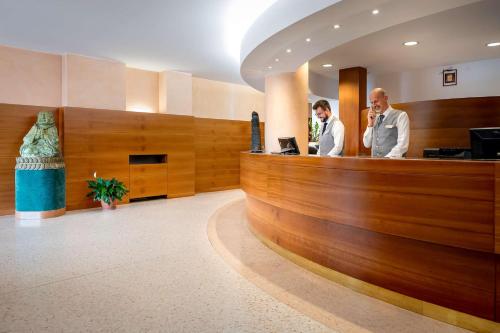 two men standing at the reception desk of a hotel lobby at Best Western Cavalieri Della Corona in Cardano al Campo
