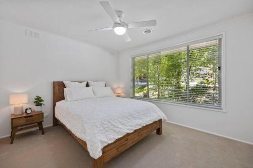 a white bedroom with a bed and a window at 5 min walk to Four Pillars! in Healesville