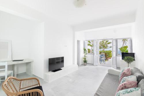 a white living room with a couch and a tv at Phaos Santorini Suites in Imerovigli