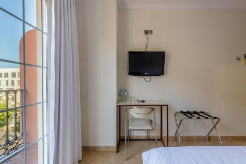 1 dormitorio con TV, mesa y silla en H-A Hotel Trebol, en Málaga