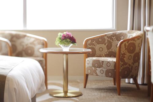 a table with a vase of flowers and two chairs at Hotel Nikko Kanazawa in Kanazawa