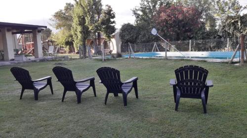 vier schwarze Stühle im Gras in der Nähe eines Pools in der Unterkunft COMPLEJO DRUMMOND en el Camino del Vino in Ciudad Lujan de Cuyo