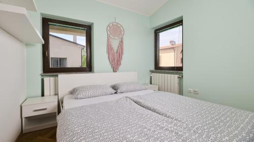 a white bedroom with a bed and two windows at Apartment Iriska in Novigrad Istria