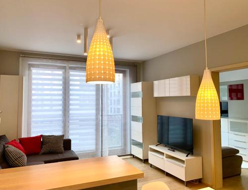 een woonkamer met een televisie en 2 hanglampen bij Project Comfort Apartament Przasnyska 7/33 Warszawa in Warschau