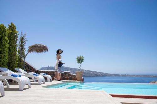 a woman standing next to a swimming pool with chairs at Oia Sunset Villas in Oia