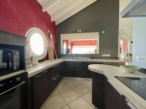 a large kitchen with a red wall and a window at Horizon bleu Caraibes in Le Moule