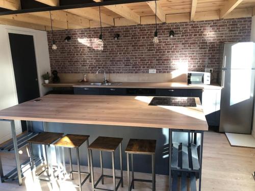 a kitchen with a large wooden counter with stools at Steen Home : Petite longère de charme in Boeschèpe