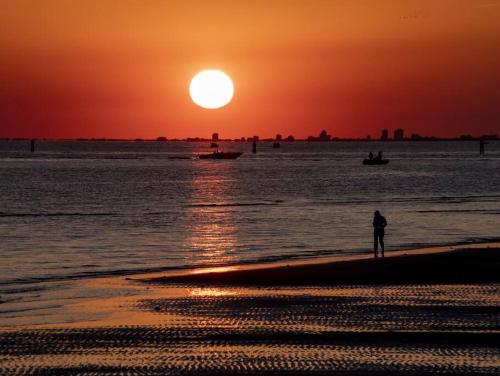 una persona in piedi sulla spiaggia che osserva il tramonto di Appartamento Grado Pineta Holidays a Grado