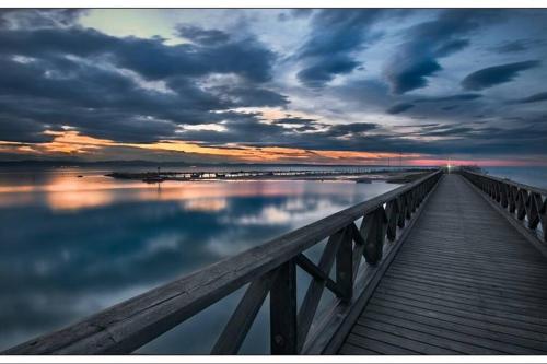 a wooden bridge over the water with a cloudy sky at Appartamento Grado Pineta Holidays in Grado