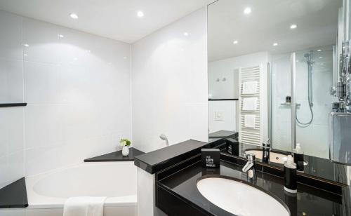 a white bathroom with a sink and a tub at The Rilano Hotel München in Munich