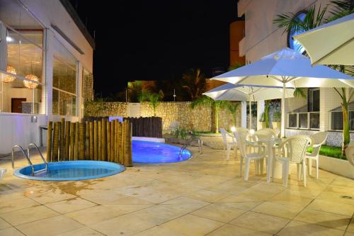 a patio with a table and an umbrella and a pool at Happy Hotel Ponta Negra in Natal