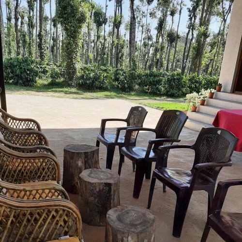 a group of chairs and tables with trees in the background at Katihalli Estate Stays in Hassan
