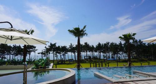 a swimming pool with palm trees and an umbrella at Ramada Plaza by Wyndham Jaeun in Sinan