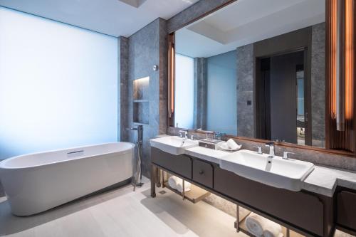 uma casa de banho com 2 lavatórios, uma banheira e um espelho grande em Radisson Blu Resort Wetland Park em Wuxi