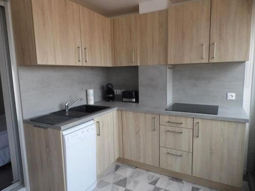 - une cuisine avec des placards en bois et un lave-vaisselle blanc dans l'établissement Appartement 3 pièces rénové, proche plage et commerces, pour 4 personnes - FR-1-326-669, à Marseillan