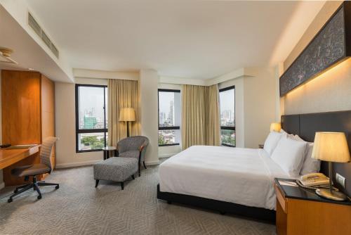 a hotel room with a bed and a desk and windows at Chatrium Sathon Bangkok in Bangkok