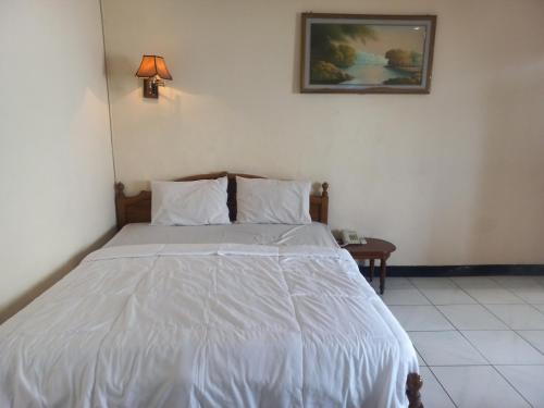 a bedroom with a white bed with a lamp and a table at Collection O 92242 Hotel Tanjung Emas in Purwokerto