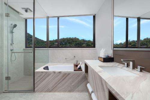 a bathroom with a tub and a shower with windows at Ascott Dadonghai Bay Sanya in Sanya