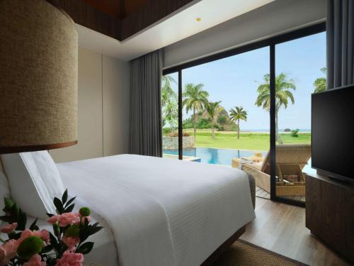 a bedroom with a bed and a view of a pool at Pullman Lombok Merujani Mandalika Beach Resort in Kuta Lombok