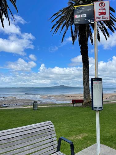 a sign sitting next to a bench next to a beach at family friendly 3BR flat - 3min walk to the beach - self contained in Auckland