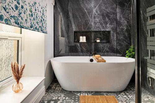 a white bath tub in a bathroom with black tiles at Finest Retreats - Peace Retreats Penthouse in Pwllheli