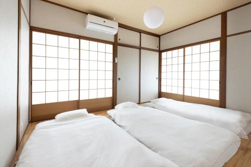 three white beds in a room with windows at The minpark in Dazaifu