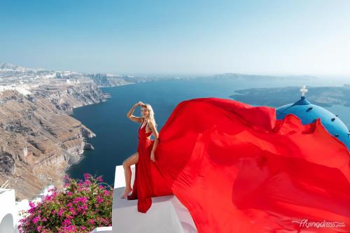 a woman in a red dress sitting on top of a cliff at Imer Villas in Imerovigli