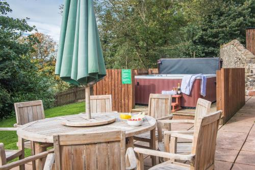 a wooden table with an umbrella on a patio at The Granary with Hot Tub in Forgandenny