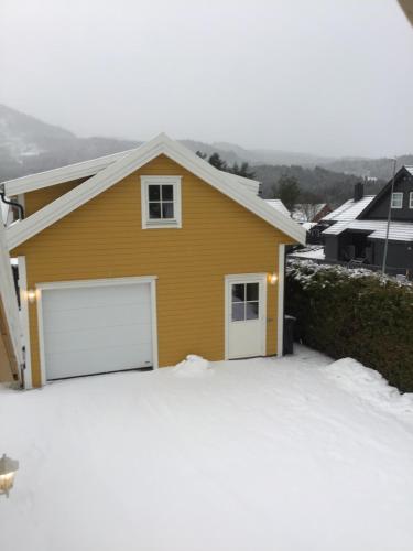 a yellow house with white garage doors in the snow at Sandvik Garasjeloft in Vossevangen