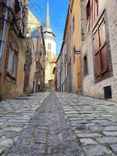 une vieille rue en pierre avec une église au loin dans l'établissement Appart hôtel Toucy, à Toucy