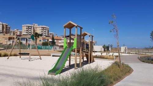 un parque infantil con un tobogán verde en la arena en Los Flamencos - Playa Paraíso - Calle Bomilcar, en Cartagena