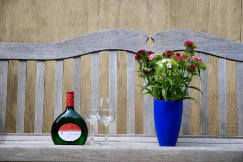 Una botella de vino y un jarrón con flores en un banco. en Biobausewein WEIN HOTEL LEBEN en Iphofen