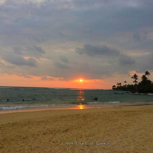 a sunset on the beach with people in the water at skyresort in Tangalle