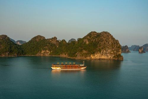 a boat in the water with mountains in the background at Nostalgia Halong Cruise in Ha Long