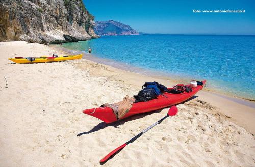 a red kayak sitting on a sandy beach next to the ocean at AFFITTACAMERE DORGALI B&B da ZIETTO in Dorgali