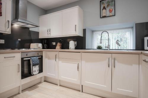 uma cozinha branca com armários brancos e uma janela em Rose Coach House - 3 Bedroom Cottage - Pendine em Pendine