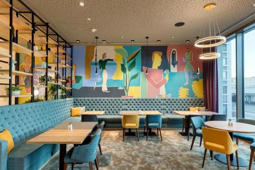 a restaurant with tables and chairs and a mural at BASSENA Wien Donaustadt in Vienna