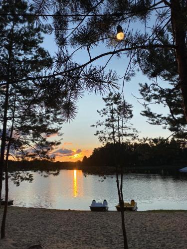 a sunset over a lake with two boats on the shore at Kempings Bejas in Babīte