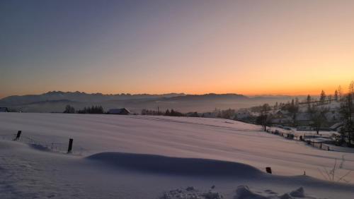 a snow covered field with the sunset in the background at Domek pod Wiśnią in Mizerna