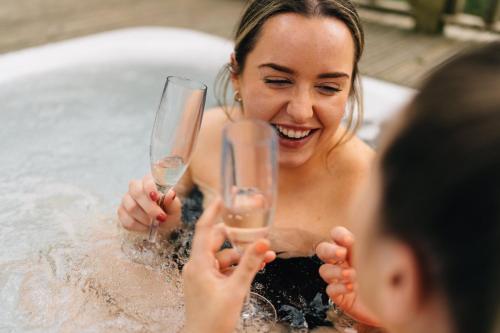 Eine Frau mit Champagner-Gläsern in einem Whirlpool. in der Unterkunft RiverBeds - Luxury Wee Lodges with Hot Tubs in Glencoe