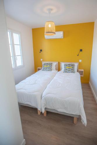 - une chambre avec 2 lits et un mur jaune dans l'établissement LE MATELOT Maison avec piscine/parking/wifi/plages 5kms, aux Mathes