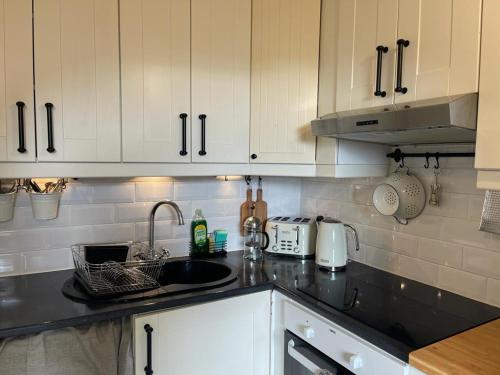 cocina con armarios blancos y encimera negra en Ashcroft Hall - Converted Chapel in Central Cirencester, en Cirencester