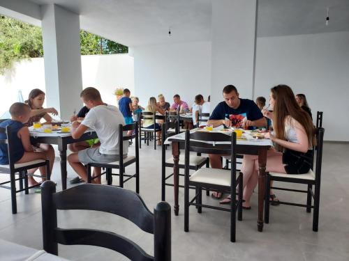 grupa ludzi siedzących przy stolikach jedzących jedzenie w obiekcie Hotel SEADEL w mieście Ksamil